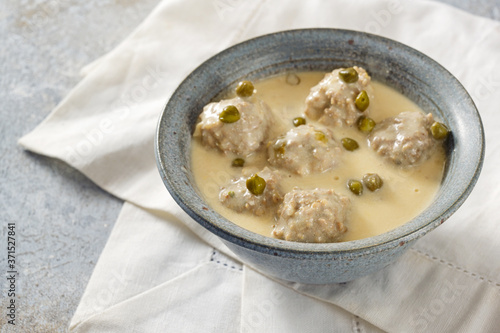 Koenigsberger Klopse or boiled meatballs in a white bechamel sauce with capers, traditional Polish and German dish in a gray bowl on a white napkin, selected focus photo