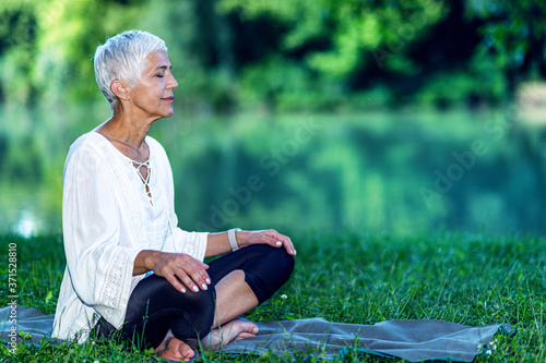 Obraz na plátně Senior woman meditating by the water