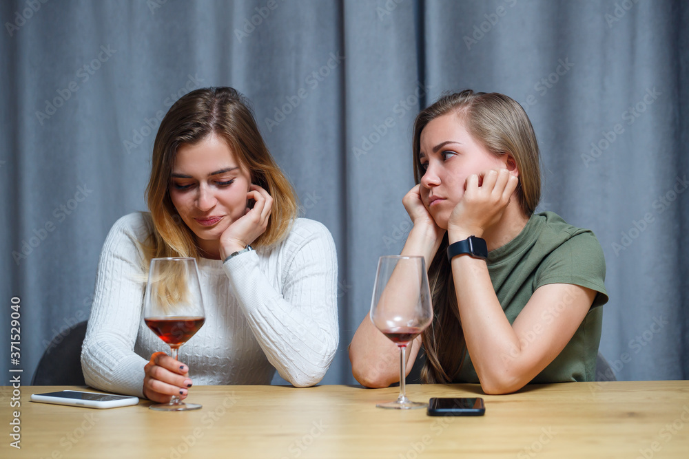 Two girls of European appearance are sitting at the table with glasses of wine. Conversation of girlfriends with alcoholic drinks. Two girls of European appearance are sitting at the table with glasses of wine. Conversation of girlfriends with alcoholic drinks.