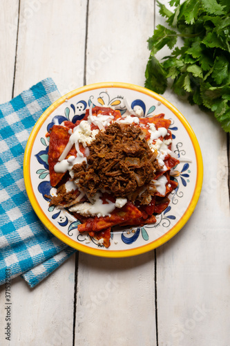 Mexican red chilaquiles with chilorio and cheese on white background photo