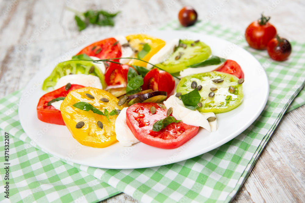 Delicious caprese salad of yellow, green and red tomatoes with cheese and fresh basil Delicious caprese salad of yellow, green and red tomatoes with cheese and fresh basil