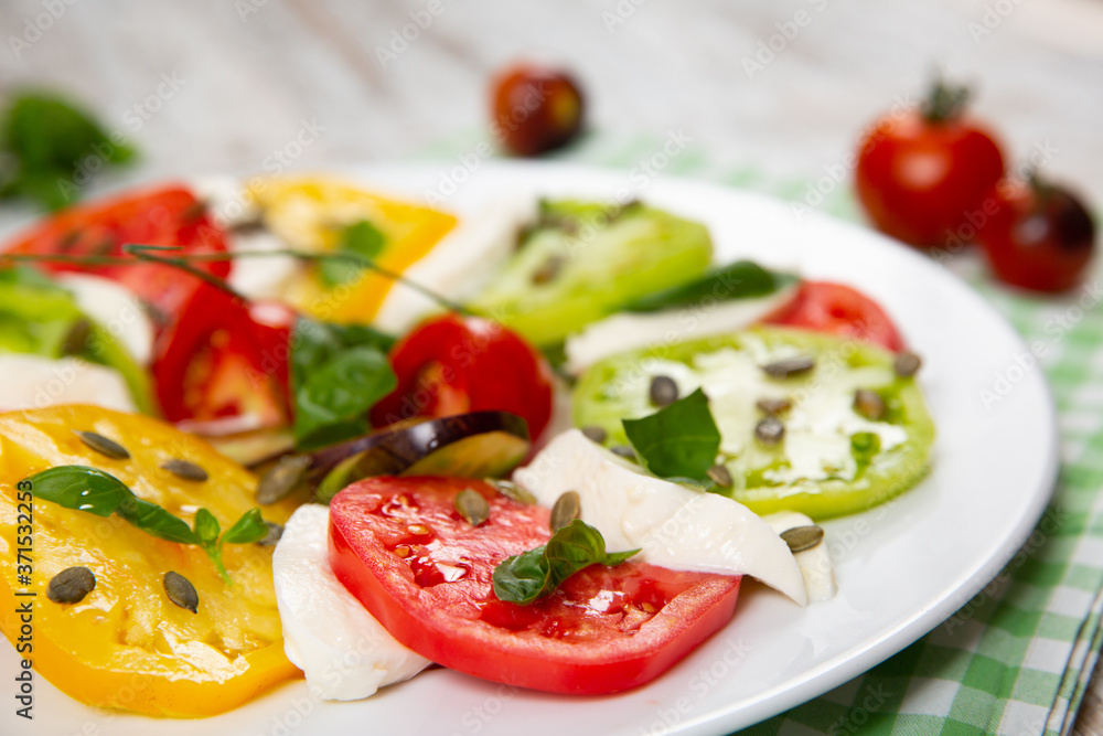 Delicious caprese salad of yellow, green and red tomatoes with cheese and fresh basil Delicious caprese salad of yellow, green and red tomatoes with cheese and fresh basil