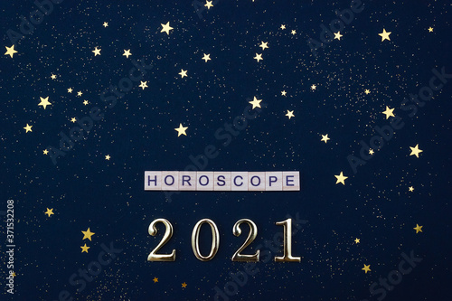 Word Horoscope and numbers 2021. Wooden blocks with letters on dark blue background decorated with golden stars confetti. Flat lay.