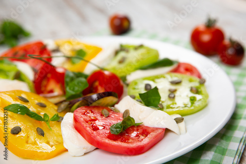 Delicious caprese salad of yellow, green and red tomatoes with cheese and fresh basil