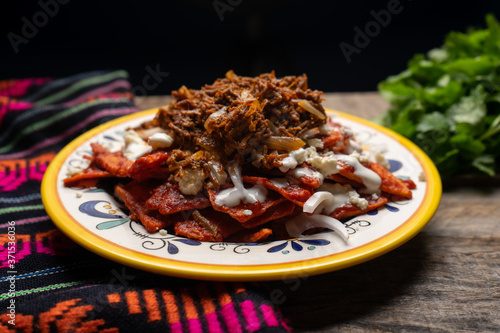 Mexican red chilaquiles with chilorio and cheese on wooden background photo