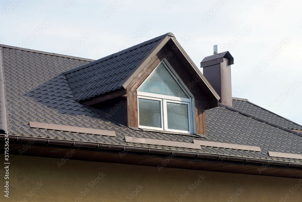 part of the roof of a private house under a tiled roof with a window against the gray sky