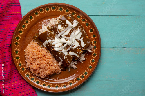 Mexican chicken enchiladas with mole sauce and rice on turquoise background photo