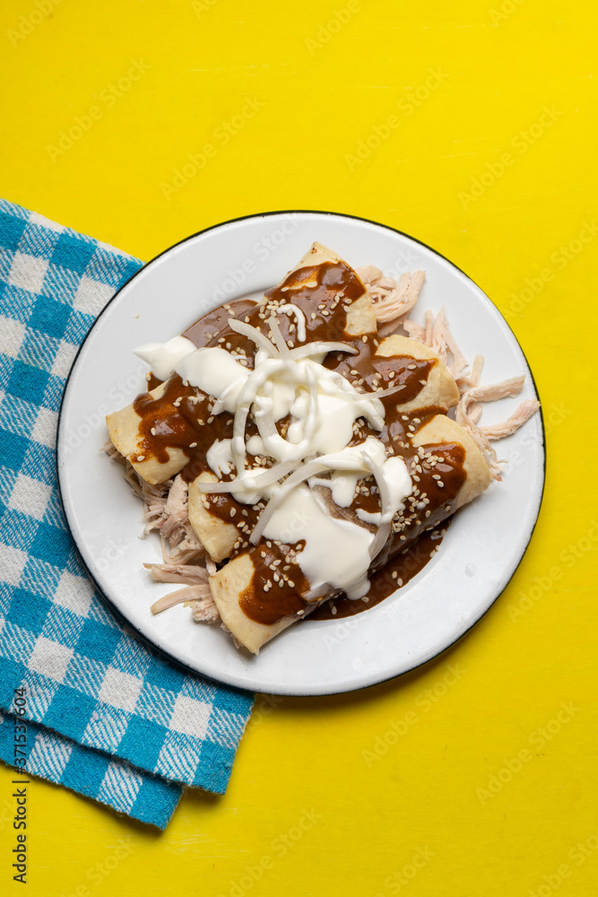Mexican chicken enchiladas with mole sauce on yellow background Mexican chicken enchiladas with mole sauce on yellow background