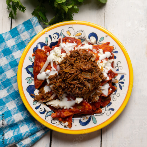 Mexican red chilaquiles with chilorio and cheese on white background photo