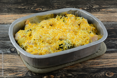 Chicken potato and broccoli casserole with shredded cheese topping in foil baking pan on potholder on table