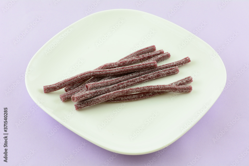 Sour blueberry candy sticks on white snack plate on lavender background Sour blueberry candy sticks on white snack plate on lavender background