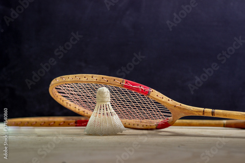 Vintage badminton racket on a black background. Badminton racket on plywood. Racket and shuttlecock on a textured black background. Vintage sport rackets with shuttlecock.