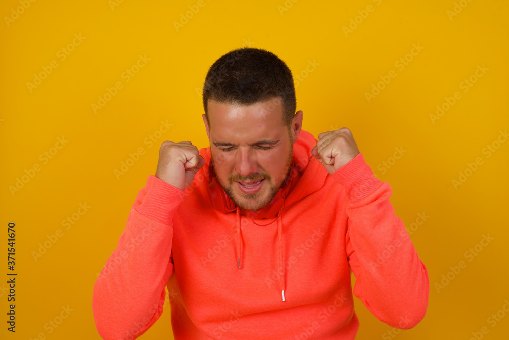 Caucasian brunette man rejoicing his success and victory clenching his fists with joy. Lucky man being happy to achieve his aim and goals. Positive emotions, feelings. Caucasian brunette man rejoicing his success and victory clenching his fists with joy. Lucky man being happy to achieve his aim and goals. Positive emotions, feelings.