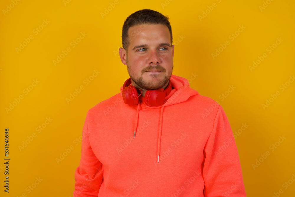 Dreamy young male with thoughtful expression, looks away keeps hands down bitting his lip thinks about something pleasant poses against gray wall. Dreamy young male with thoughtful expression, looks away keeps hands down bitting his lip thinks about something pleasant poses against gray wall.