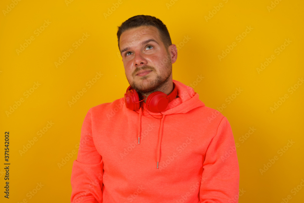 Portrait of mysterious charming blond male looking up with enigmatic smile. Handsome smiling guy looking up standing against gray wall. Portrait of mysterious charming blond male looking up with enigmatic smile. Handsome smiling guy looking up standing against gray wall.