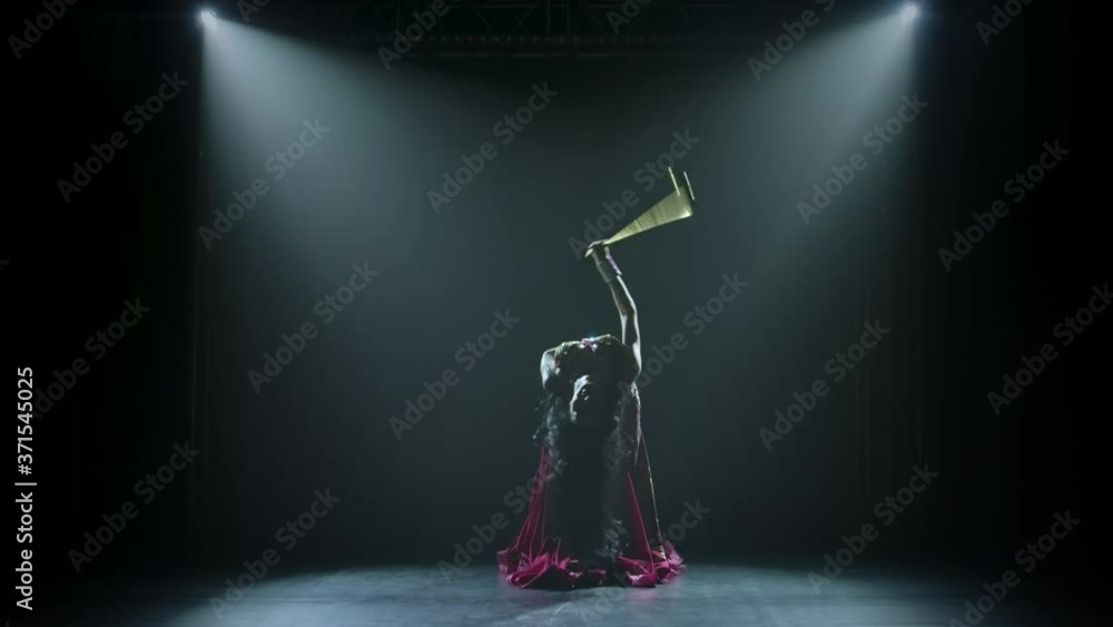 Alluring traditional oriental belly dancer girl dancing with a golden cane on neon lighting background and smoke. Silhouettes of a slender flexible body.