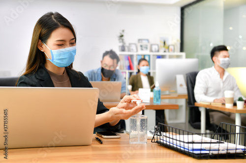 Asian woman washing hands sanitizer gel and wearing face mask working in new normal office and doing social distancing during corona virus covid-19 pandemic