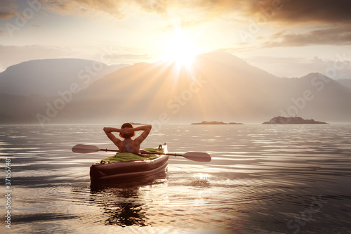 Woman relaxing on her kayak during a colorful summer sunset. Taken in Howe Sound, North of Vancouver, British Columbia, Canada.