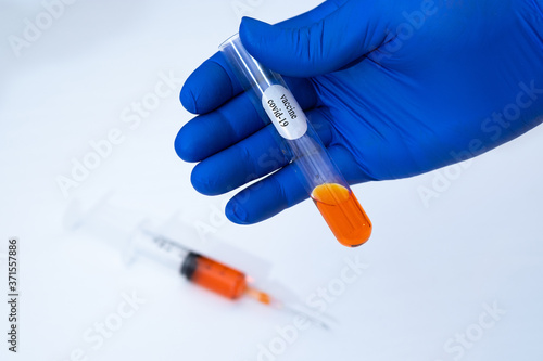 Scientist with blue glove and pick up the Scientific orange color solution for chemical analysis. vaccine covid-19 concept.