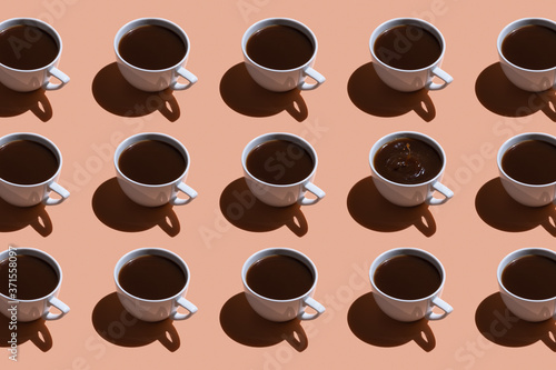 White cups with black coffee on a beige background. pattern with hard light. A splash of coffee in one cup.