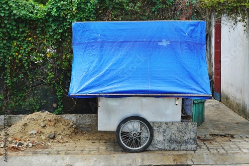 Wheeled cart covered with funky blue tarp parked on the sidewalk in urban Vietnam