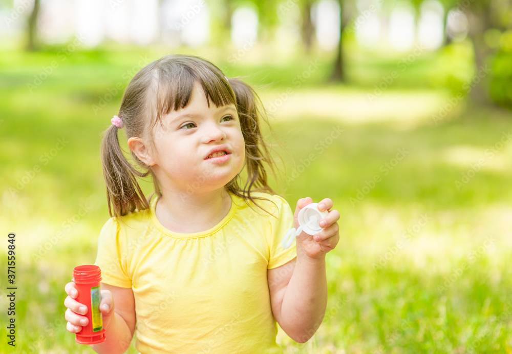Happy girl with syndrome down blows bubbles in a summer park