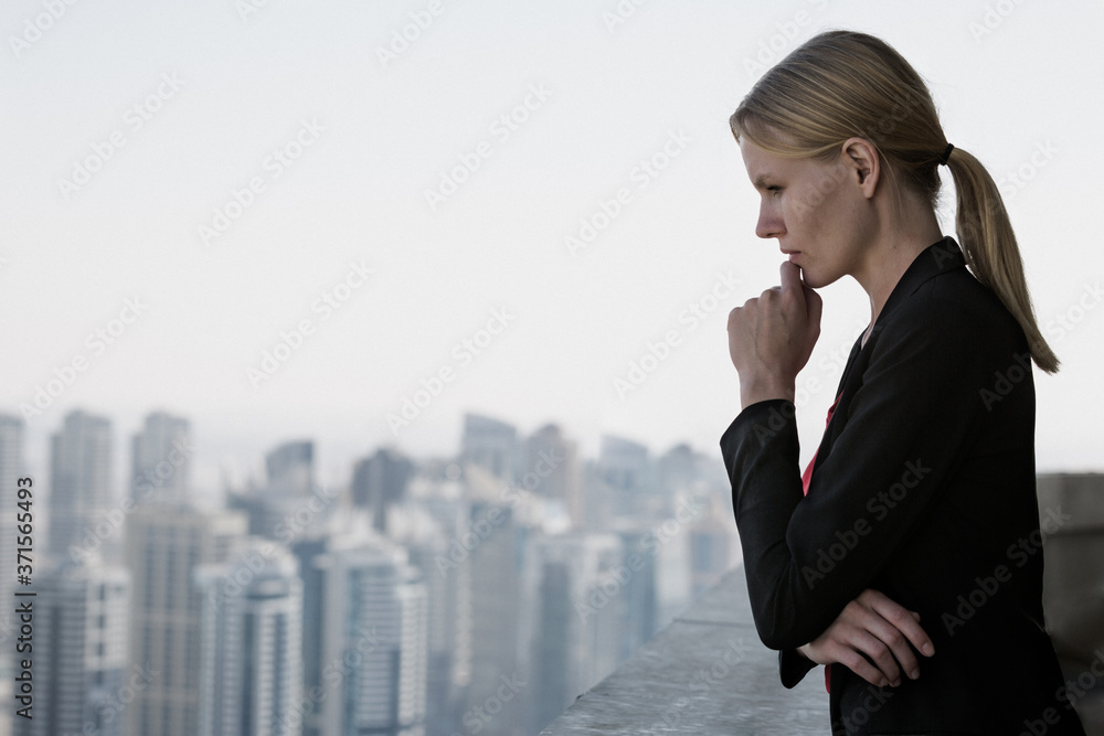 Business challenge and career opportunities. Concerned businesswoman in suit contemplating future decisions with hand on chin at work while looking at the modern city view in the background.