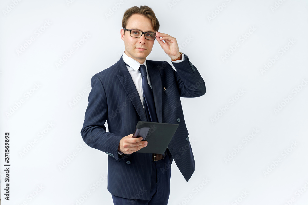 Portrait of a businessman in a blue suit who is holding an electronic tablet in his hands and adjusting his glasses. White background. Portrait of a businessman in a blue suit who is holding an electronic tablet in his hands and adjusting his glasses. White background.