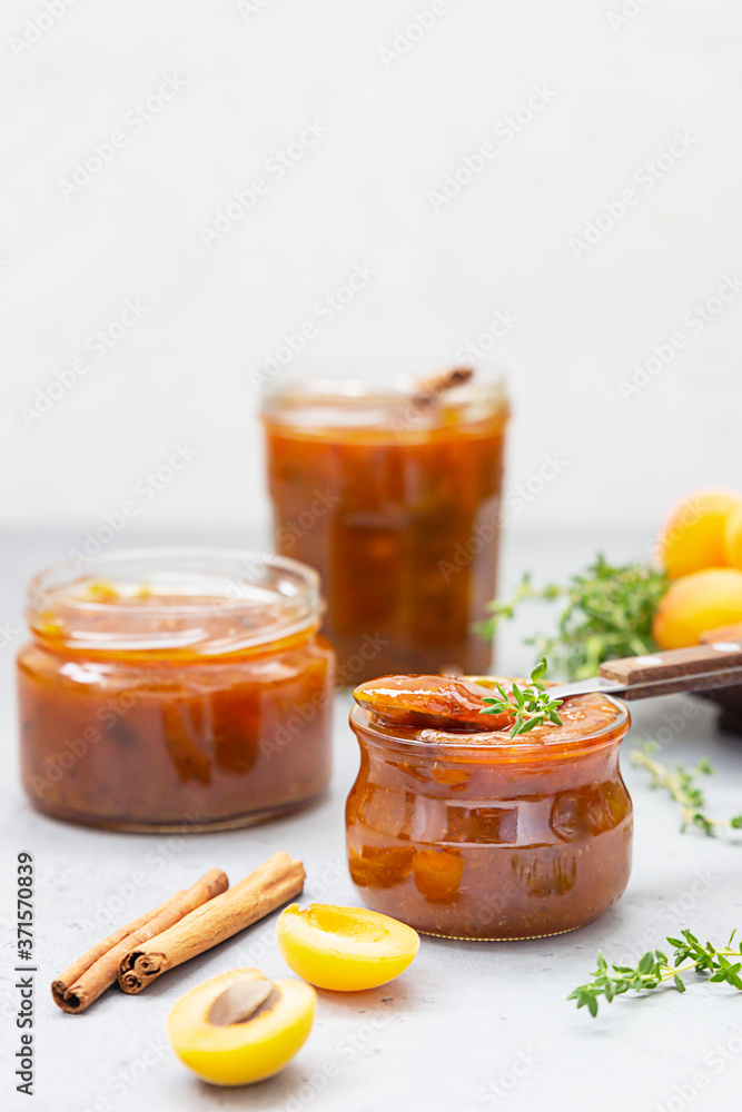 Homemade organic apricot jam in glass jars, ripe apricots, cinnamon and thyme on grey background. Homemade organic apricot jam in glass jars, ripe apricots, cinnamon and thyme on grey background.
