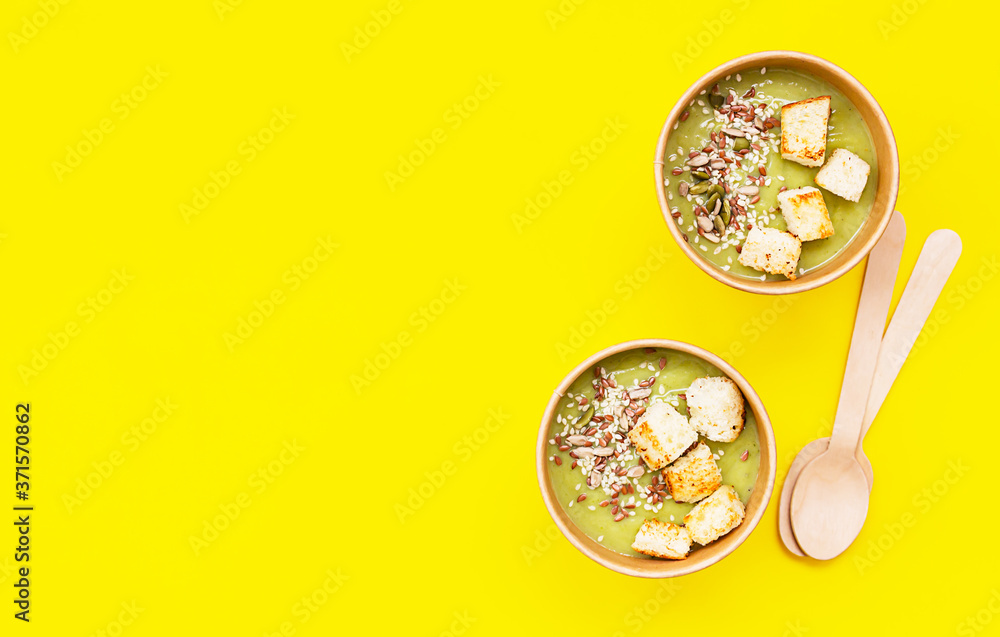 Fresh broccoli cream soup with croutons and seeds in craft containers on yellow background. Soup to go, healthy food delivery. Fresh broccoli cream soup with croutons and seeds in craft containers on yellow background. Soup to go, healthy food delivery.