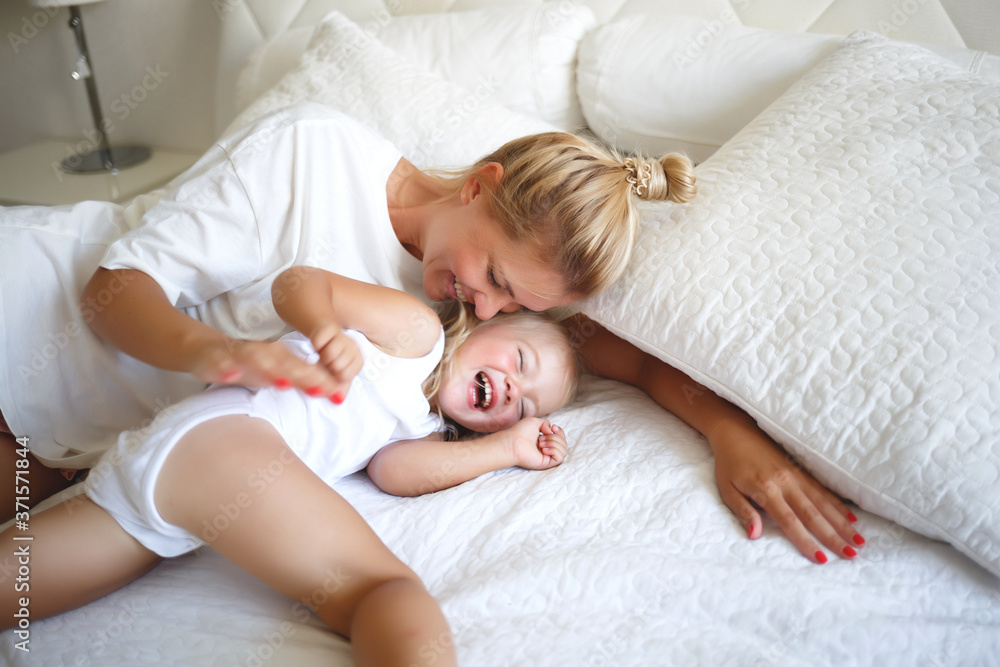 young woman hugging with her daughter on a white bed young woman hugging with her daughter on a white bed