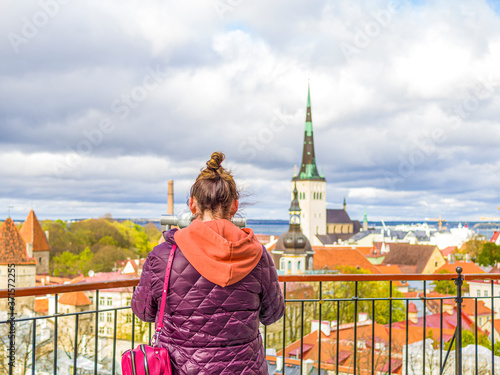 Tourist in Estonia  taking photo of old town with smartphone. Travel photography with mobile phone. travel and photography concept  young beautiful woman in red looks towards city towers. copy space