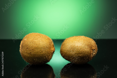 several kiwis on dark glass with green glare on green background