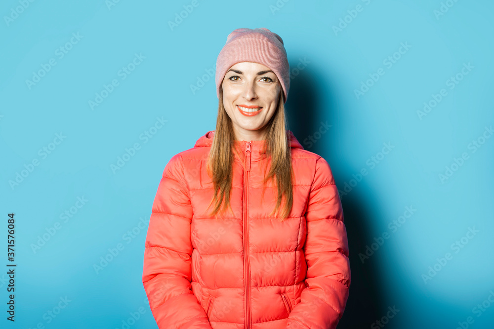 Beautiful Young woman in a hat and a winter jacket on a blue background. The concept of the onset of cold weather, winter, change of season Beautiful Young woman in a hat and a winter jacket on a blue background. The concept of the onset of cold weather, winter, change of season