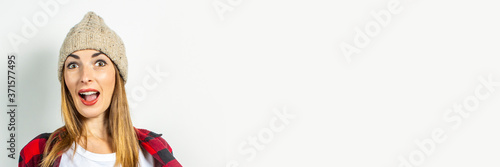 Young woman with a surprised face in a hat, a red shirt and a white T-shirt on a white background. Stylish, winter concept, teenager style, shock, surprise. Banner