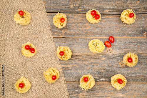 Nests of tagliatelle noodles with egg-shaped mini roma tomatoes on a rustic wooden table with burlap