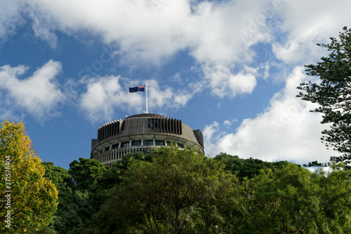 Fotografie The Beehive above the treeline - New Zealand parliament building with flag flying on a sunny day