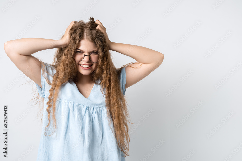 Fototapeta premium Photo of beautiful girl with curly long hair and in round spectacles, holding hands on head