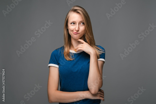 Thoughtful young woman stands with her chin in her hand, gazing thoughtfully into the distance