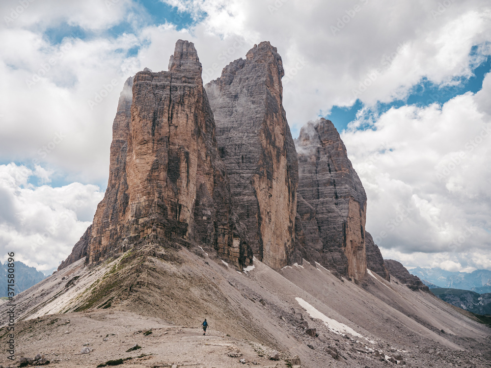 Impressive peaks of Tre Cime di Levaredo in Dolomites, Italy, with one hiker standing at the base of the mountain, which shows the scale