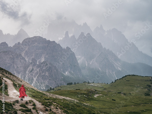 Hiker in a red poncho walking in dramatic landscape of Tre Cime national park in Dolomites, Italy, with jagged peaks of Cadini di Misurina mountain group on background