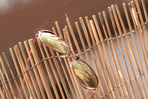 Sunglasses for ladies with big round lens hanging on bamboo fence reflecting the sun. Selective Focus