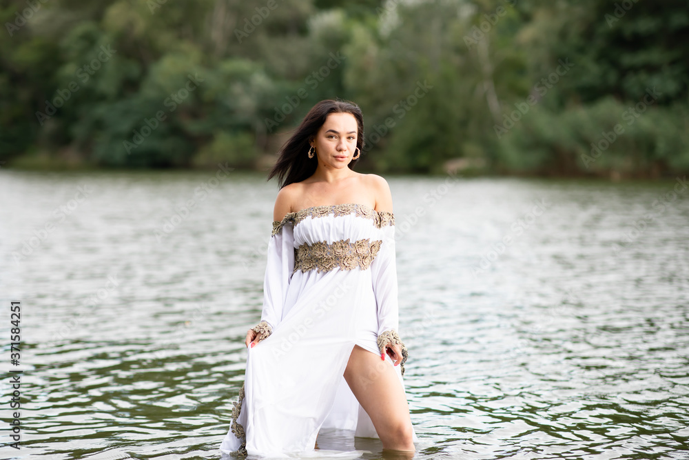 Young european woman with brown hair dressed a long white wedding dress stays in the river Young european woman with brown hair dressed a long white wedding dress stays in the river