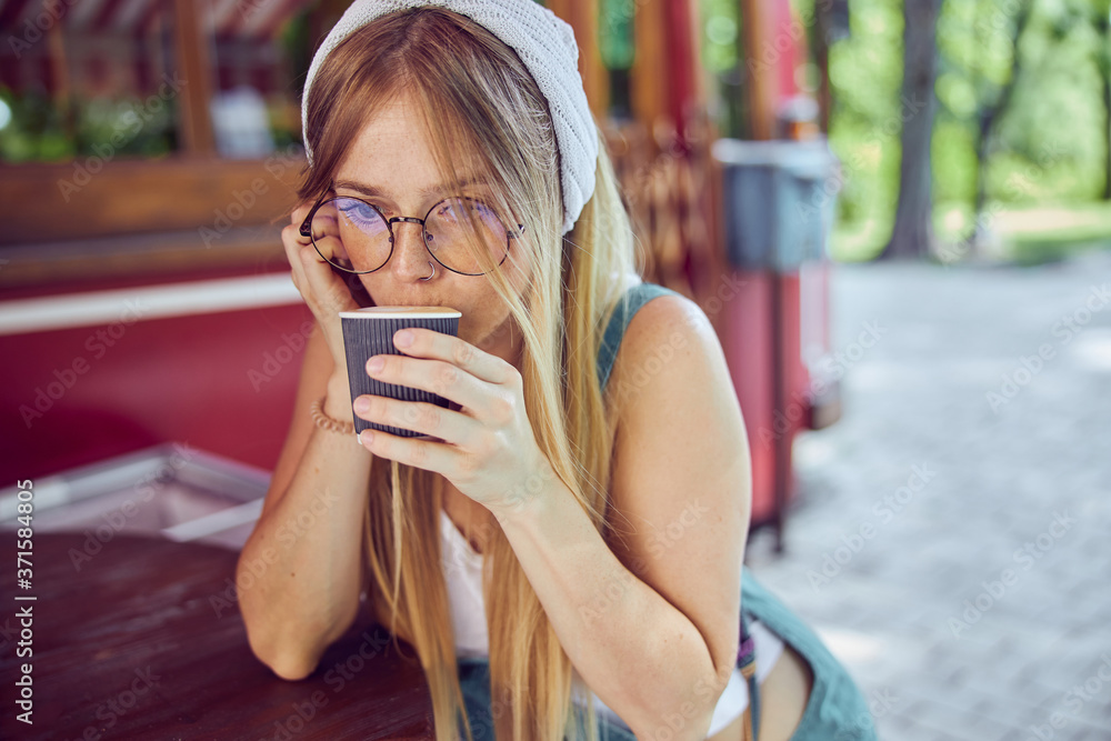 Fototapeta premium Pretty red-haired girl in glasses drinking coffee in cafe