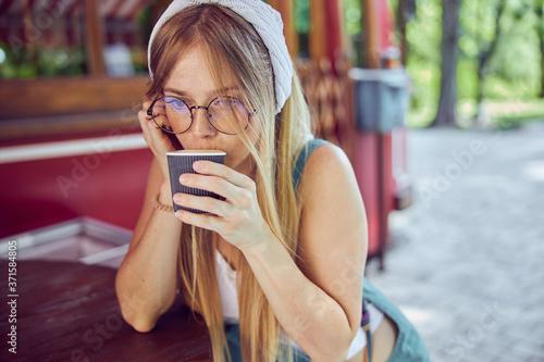 Pretty red-haired girl in glasses drinking coffee in cafe photo