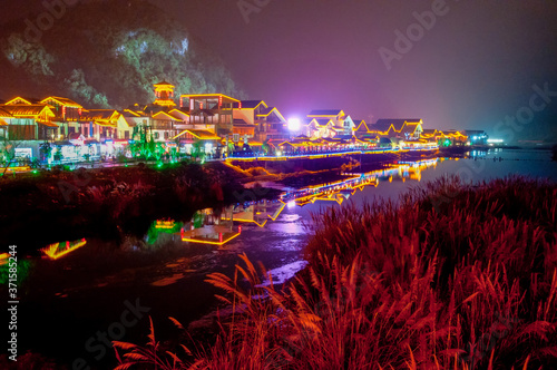 Fototapeta Naklejka Na Ścianę i Meble -  Night scene of Xibu Street, Zhangjiajie, Hunan, ,with stilted buildings, ancient buildings, streets, rivers and lights, orange sky and reflection as the background, brilliant effect, concept of: gorge