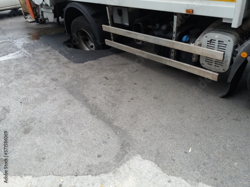 Manto stradale collassato sotto il peso di un camion, con la ruota incastrata nella buca photo