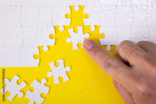 Hand putting the a piece of white jigsaw puzzle on color background