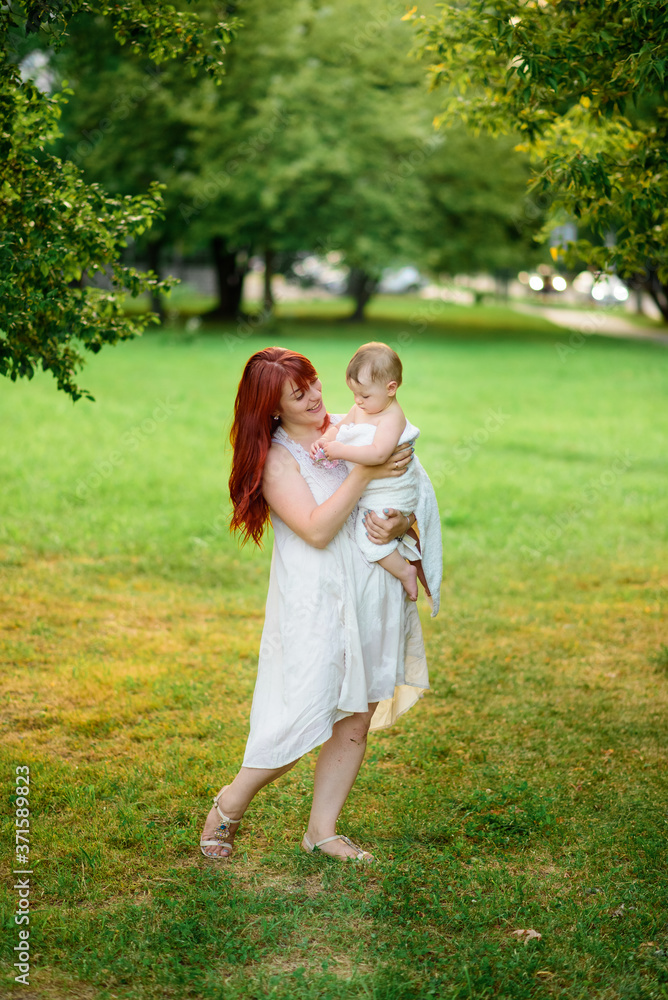 Fototapeta premium Mom hugs and plays with her one-year-old daughter wrapped in a towel after bathing.