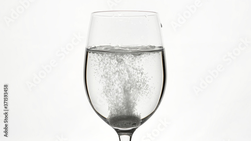 pill of effervescent aspirin in elegant glass with water, white background